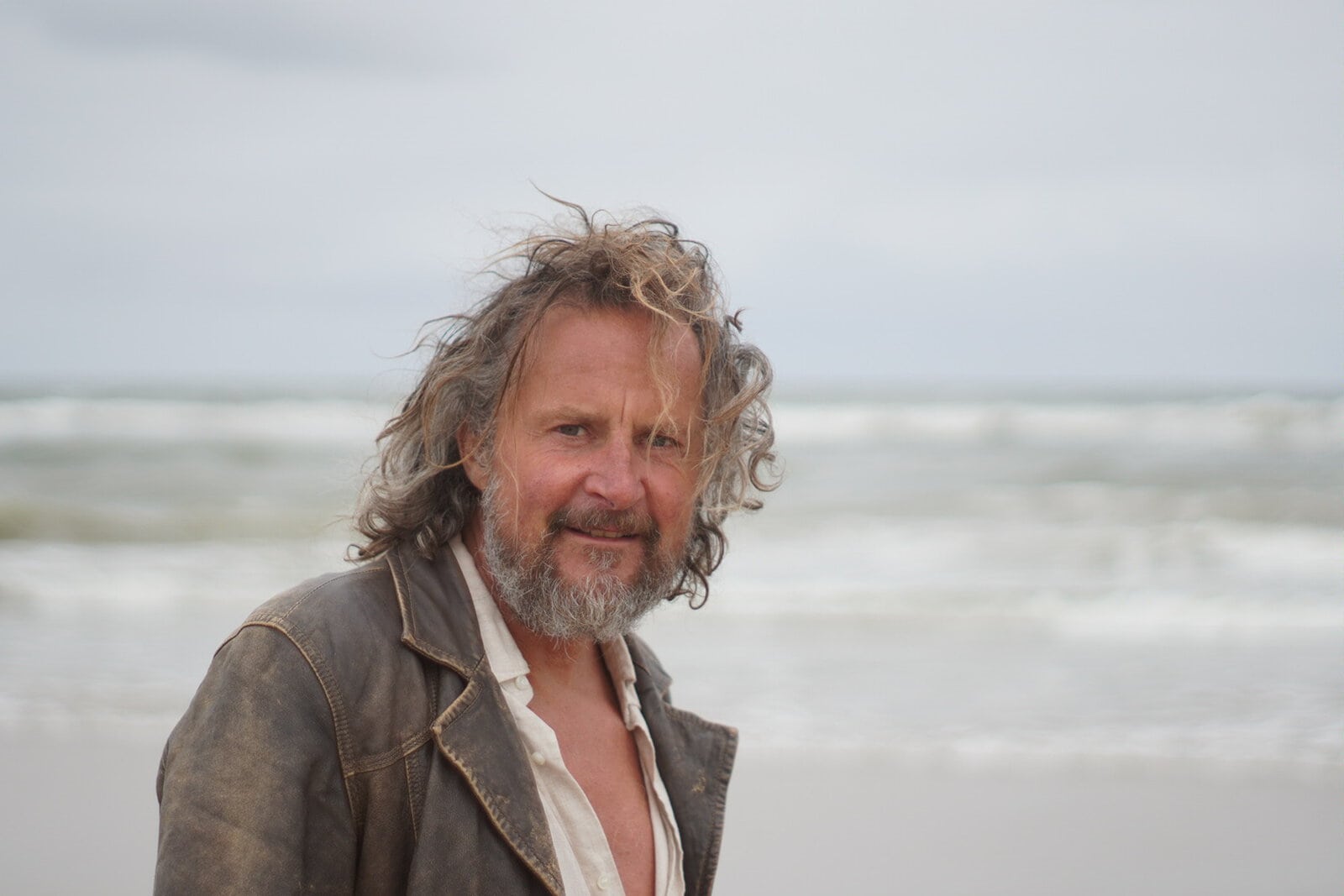 Portret van Bart van Broekhoven op het strand met zee en golven op de achtergrond.