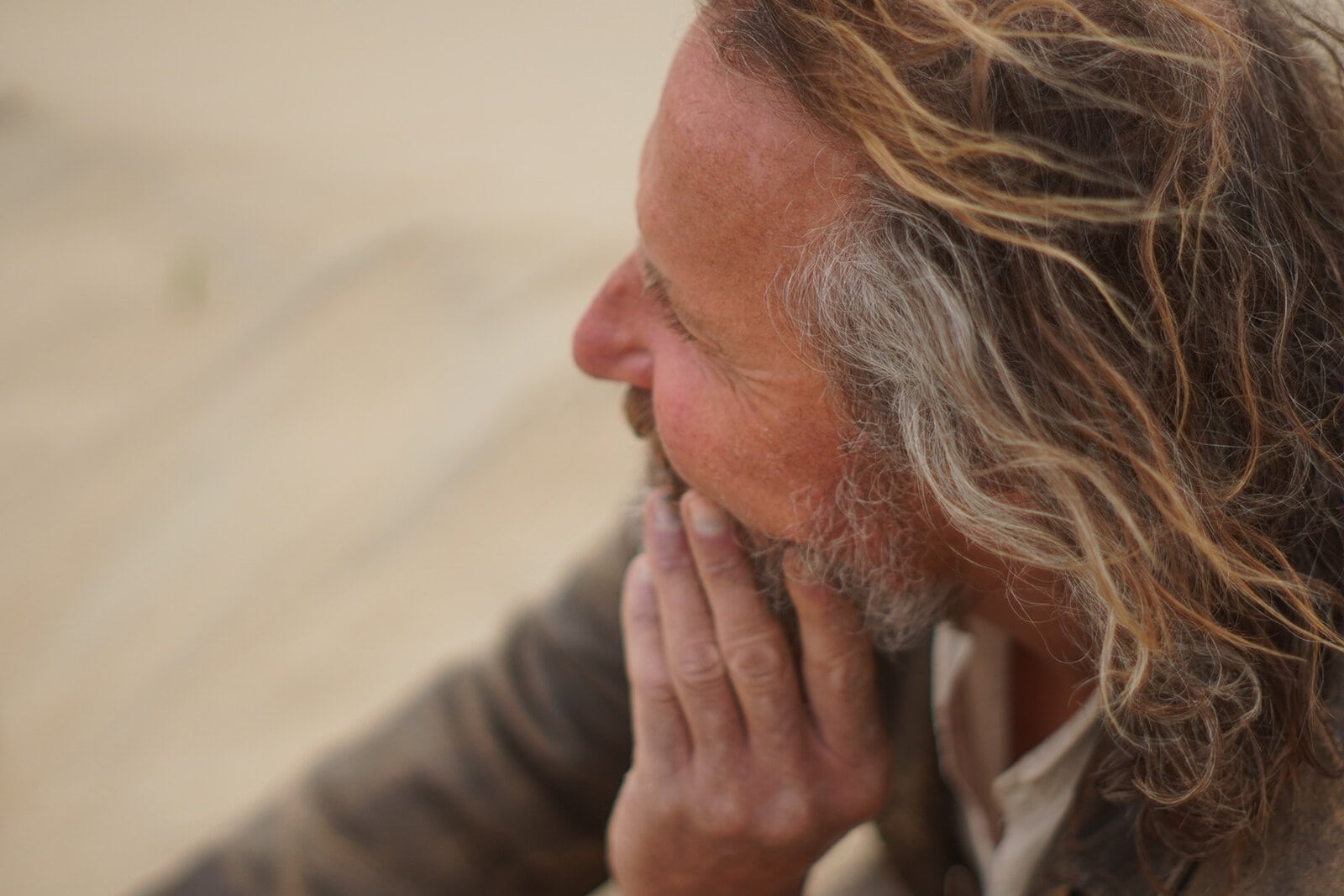 Man met lang, golvend haar en grijze baard, glimlachend in gedachten.