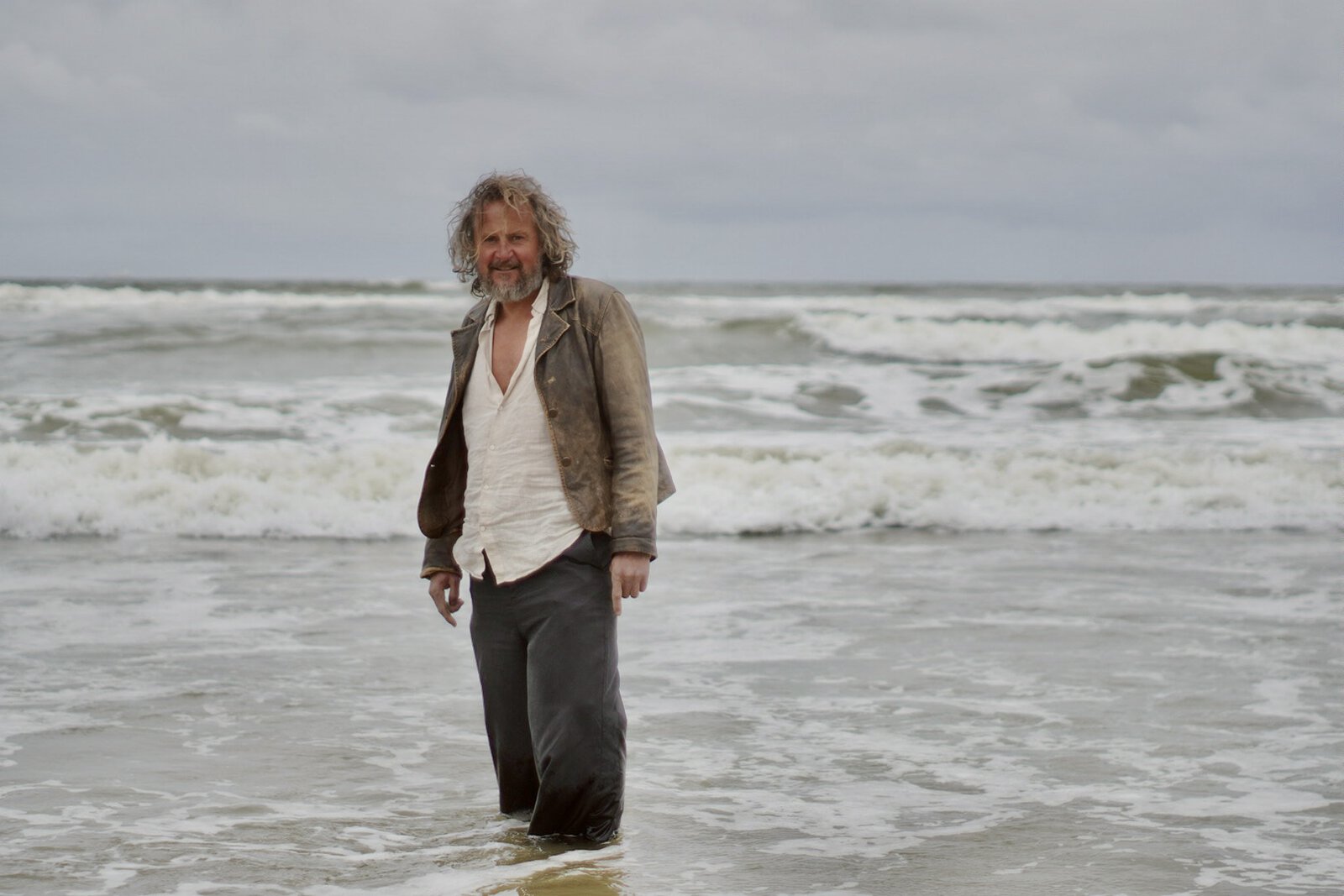 Bart van Broekhoven wandelt op het strand met golven op de achtergrond.